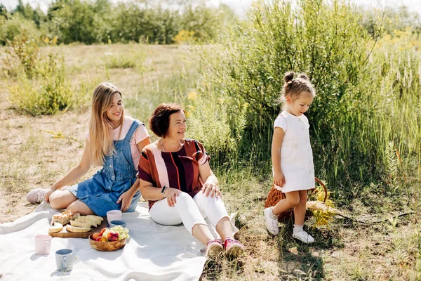 Een grootmoeder en haar twee kleindochters picknicken in de natuur, brengen samen tijd door in het weekend. — Stockfoto