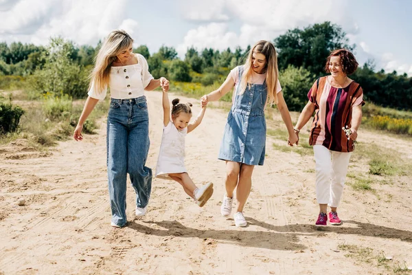 Várias gerações de mulheres da mesma família estão caminhando ao longo de uma estrada de terra fora da cidade, aproveitando o tempo passado juntas — Fotografia de Stock