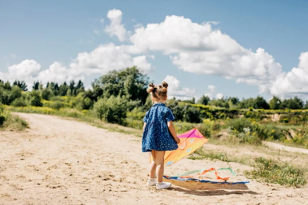 Una niña está volando una cometa en un camino de campo fuera de la ciudad. Infancia, alegría, cuidado —  Fotos de Stock