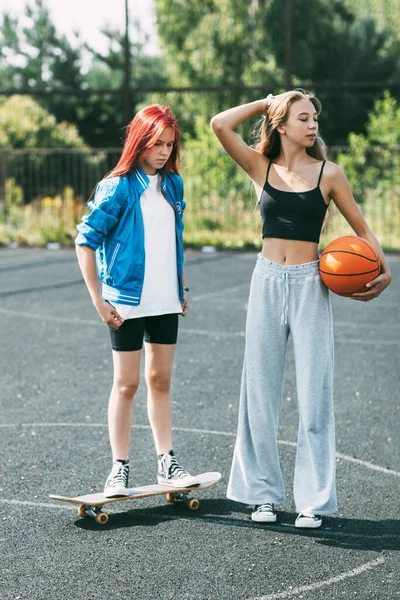 Porträt zweier Teenager-Mädchen mit Basketball und Skateboard auf einem Sportplatz — Stockfoto