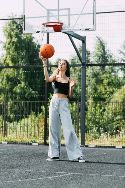 Seorang gadis remaja yang cantik melempar bola basket selama latihan di lapangan olahraga atau stadion sekolah — Stok Foto