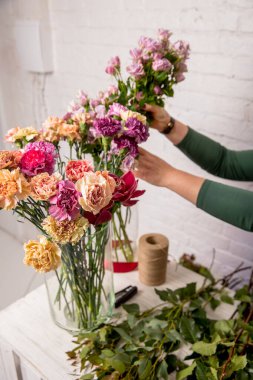 Çiçekçinin işyeri. Beyaz tuğla bir duvarın arka planına karşı masada çalışmaya başlamadan önce aletler ve çiçekler. Bir çiçekçi buket için bir çiçek seçer. Özel ders. Adım adım..