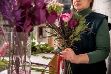 Çiçekçinin işyeri. Çiçekçi bir buket gül, karanfil ve okaliptüs yapar, adım adım çiçek ekler. Özel ders. Yatay fotoğraf