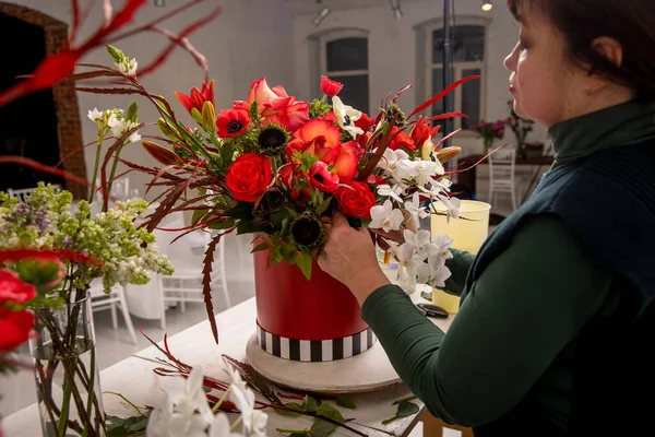 Florist workplace on the background of a white brick wall. The florist composes a bouquet of orchids, roses, sunflowers, lilies, alstemeria and ornithogalum, adding flowers to it step by step. Manual.