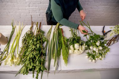 Çiçekçi güller, leylaklar, kallalar, karanfiller, ortancalar, brasica, alstroemeria, ornithogalum, thuja ve dracaena çiçeklerinden oluşan bir düzenleme yapıyor. Çiçekçi masaya çiçek koyar. Öğretici.