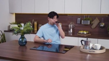 Gülümseyen Vietnamlı adam ev mutfağında sesli mesaj kaydediyor. Mutlu genç adam telefonu sosyal ağ ve ses kontrolü için kullanıyor. Orta çekim, yavaş çekim 4k