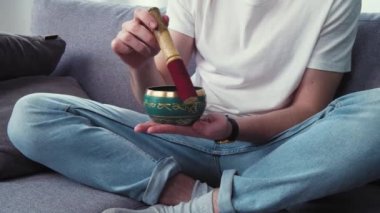 Depresyon ve stresle baş etmek. Genç adam oturma odasında Tibet çan kupasıyla şarkı söylüyor. Akıl sağlığı hakkında konuşmak, akıllı telefon uygulaması kullanmak. Yavaş çekim 4k