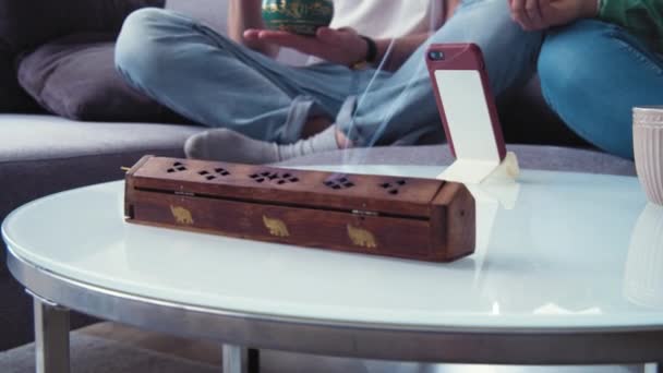 Indické tyčinky od kadidla na stole v obýváku. Rodina se učí meditovat s mobilní aplikací, starat se o duševní zdraví. Používám tibetskou mísu, stojící zvonek. Koncept klidu. Zpomalený pohyb 4k — Stock video