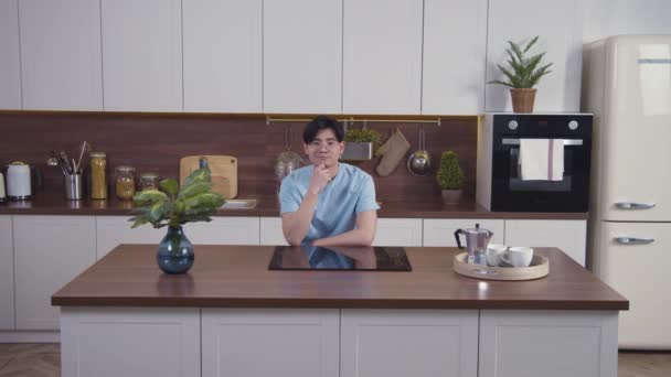 アジアの穏やかな男の肖像画笑顔と近代的なキッチンで、カメラを見て座っている。中射、スローモーション4k — ストック動画
