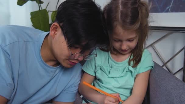 Asyalı baba ve beyaz kız ellerine resim çiziyor. Çocuk kızla mutlu aile eğlenceleri. Sevimli çocuk ailesiyle eğleniyor. Baba ve anaokulu kızı etkinliğin tadını çıkarıyorlar. 4k ağır çekim — Stok video
