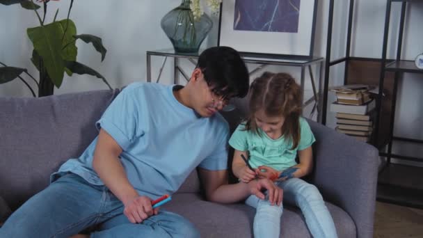 Asiatiska far och kaukasiska dotter ritar bilder på händer. Glad familj fritid med barn flicka. Söt unge som har kul med föräldrar. Pappa och förskoledotter gillar aktivitet. 4k slow motion — Stockvideo