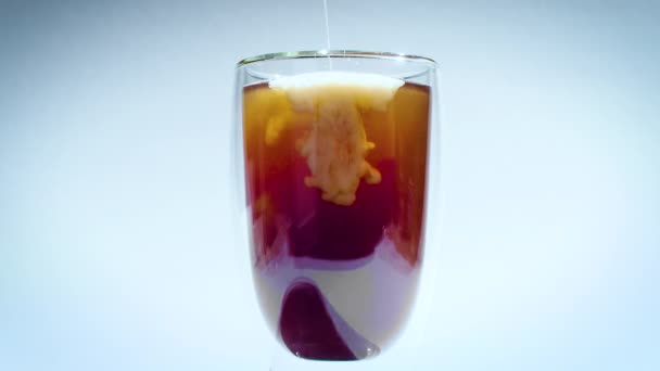 Mléko se rozpouští v kávě nebo černém čajovém nápoji. sklo s dvojitými stěnami na bílém pozadí. — Stock video