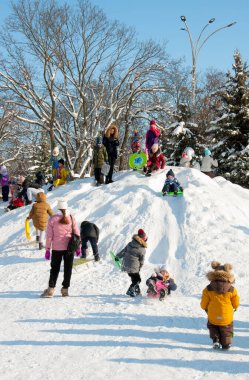 Pryluky, Chernihiv, Ukrayna - 02 / 15 / 2021: Çocuklar şehir meydanında aileleriyle birlikte kar kaydırağına biniyorlar. Güneşli kış günü