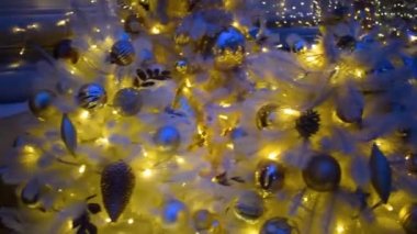 Gümüş süslemeli beyaz Noel ağacı ve gece şehrinde asılı duran altın ampuller. Kamera, odağını kaybetti. Açık havada parlayan süslü yeni yıl ağacı.