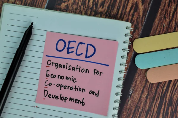 OECD - Organisation for Economic Co-operation and Development write on sticky notes isolated on Wooden Table.