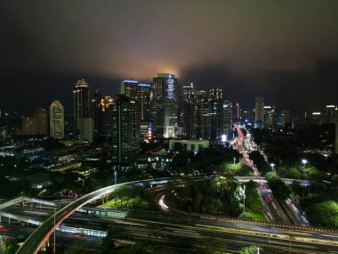 Geceleri büyük, modern bir şehrin göz kamaştırıcı gece silueti. Semanggi, Jakarta, Endonezya. Gürültü bulutlu gökdelenler ve otobanlar üzerinde hava manzarası. JAKARTA - Endonezya. 4 Şubat 2021