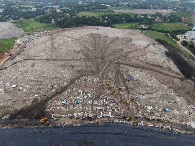 Hava görüntüsü. Dağ gibi büyük çöplükler. Traktör, 15 Şubat 2021 'de Bekasi - Endonezya' da yağmur ve şehir manzarası üzerine gürültü bulutu ile çöpleri topluyor.