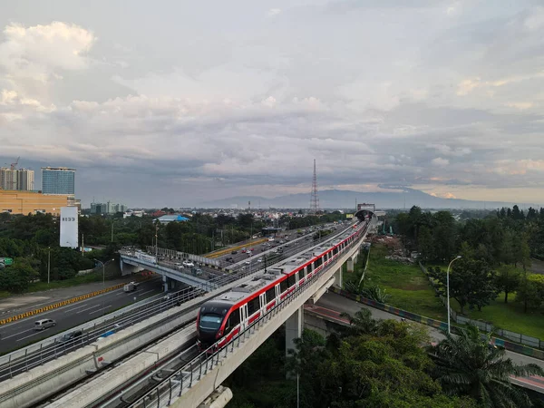 LRT, Monorrail hareket halinde Cibubur istasyonunda hızla çekiliyor. Trafiğin arka planı, dağ ve gökyüzü. Jakarta, Endonezya - 25 Mart 2021