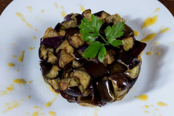 Beyaz tabakta sarı vişneli domates kreması üzerinde doğranmış patlıcan tabağı. Ahşap arka. Seçici odak.