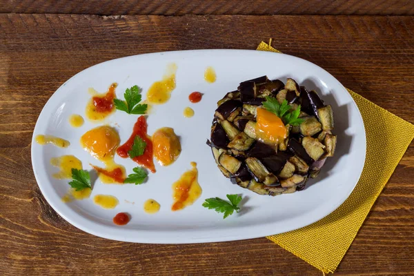 Beyaz bir tabakta sarı ve kırmızı kiraz domatesli krema üzerine doğranmış patlıcan. Ahşap arka. Seçici odak.