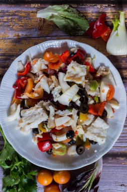 Kış kiraz domatesleri, siyah zeytin, kereviz, soğan, ahşap zemin üzerinde salamura biber ile haşlanmış morina balığı. Seçici odak.