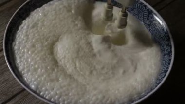 4000 kez çırpılmış krema. Video, ahşap bir arka planda kremayı mavi bir kasede çırpan aletin kırbaçlarını gösteriyor.