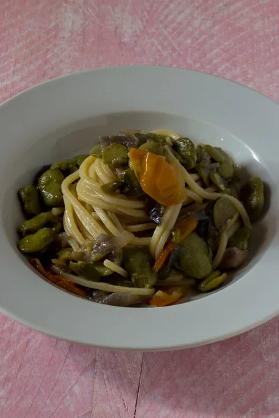 Geniş fasulyeli spagetti, soğan ve sarı vişneli domates.