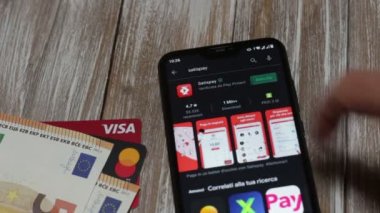  Satispay uygulamasının akıllı telefon ekranındaki Google Play Store 'a kurulumu. Arka plandaki para ve banka kartlarında.