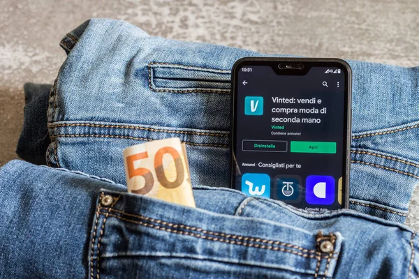 Vinted uygulama, uygulamanın google oyun mağazasından kurulumu. İkinci el giysiler. Arka planda kot pantolon ve 50 Euro..