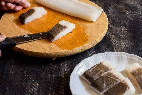 Yaşlı bir kadının elleri kesme tahtasındaki bıçakla balık filetosu kesiyor.