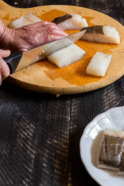 Yaşlı bir kadının elleri kesme tahtasındaki bıçakla balık filetosu kesiyor.