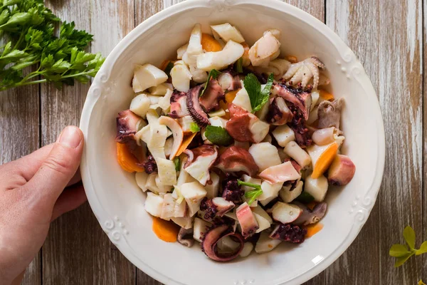 Deniz ürünleri salatası ahşap arka planda porselen kasede servis edilir.