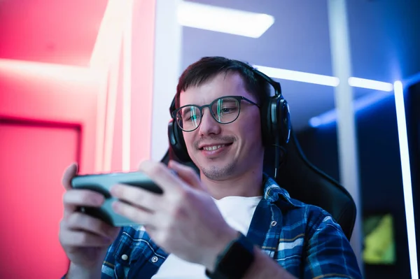 Schöner junger Mann spielt mit seinem Smartphone im neonfarbenen Raum — Stockfoto