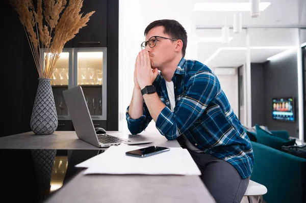 Evden bilgisayarla uzaktan çalışan düşünceli genç bir iş adamının portresi.