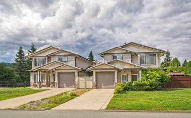 Beton garaj yolu ve önünde yeşil çimenliği olan çift katlı bir bina.