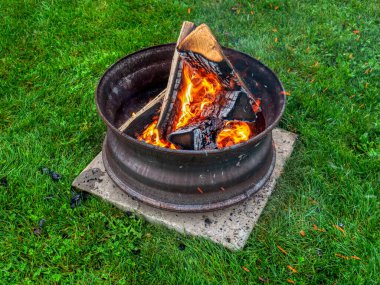 Campfire in a steel wheel on the concrete base and green lawn