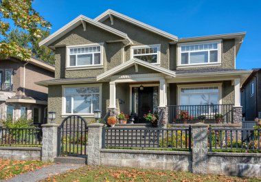 Taş ve metal çitlerin arkasında büyük ön bahçesi olan modern lüks bir ev.