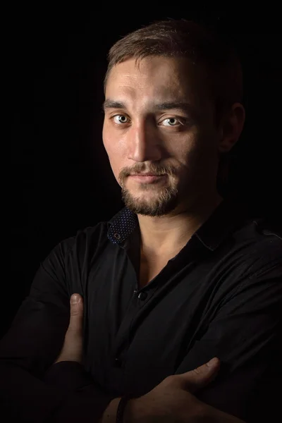 Closeup portrait of handsome man with a beard in black shirt. Isolated on black background.