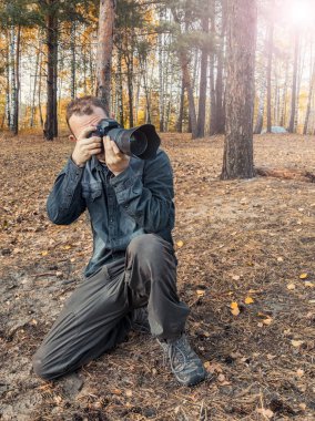 İnsan sonbahar ormanında yerde büyük siyah bir kamerayla oturur ve güneş ışınlarındaki sonbahar manzarasına bakar..