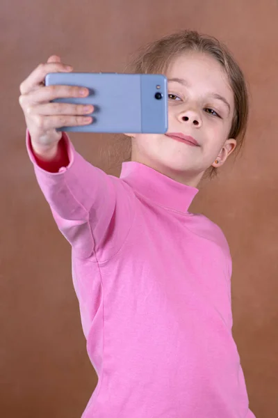 Bulanık Kahverengi Arka Planda Selfie Çeken Neşeli Küçük Bir Kızın — Stok fotoğraf