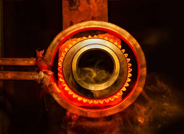 closeup calcining hot metal steel gear parts in a factory induction furnace with smoke and flame