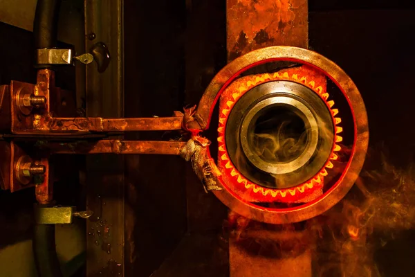 closeup calcining hot metal steel gear parts in a factory induction furnace with smoke and flame