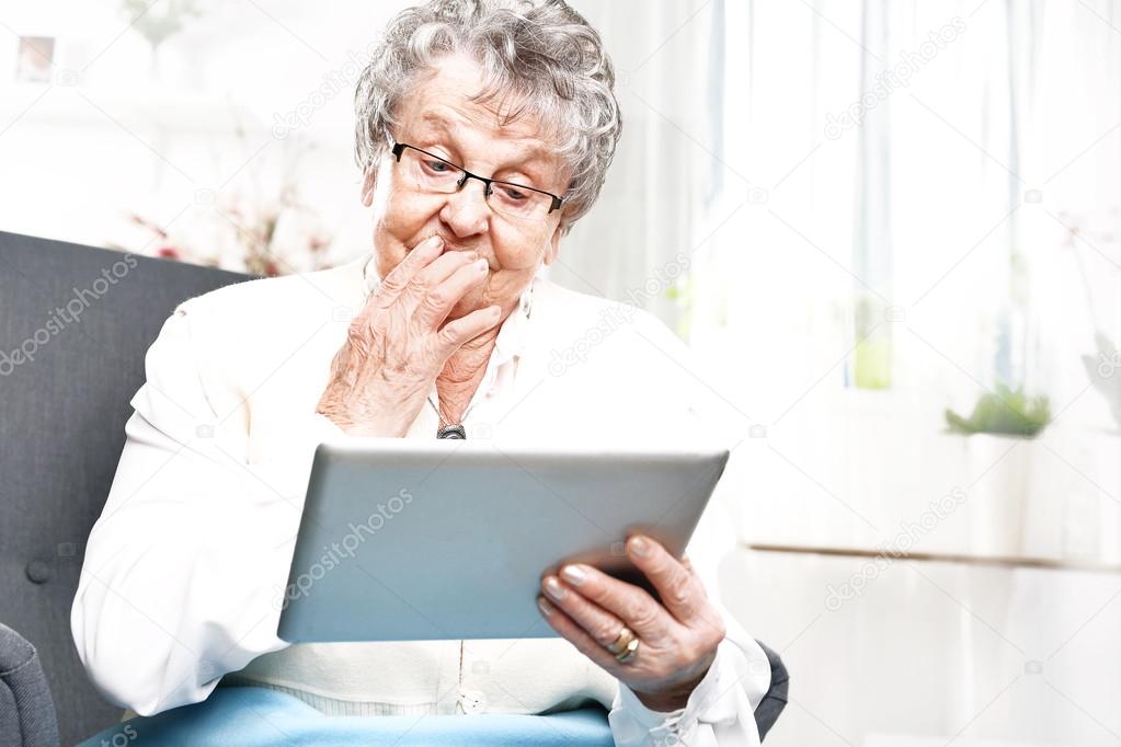 Surprised elderly woman looks in the tablet screen