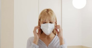 Yüzüne koruyucu maske takan bir kadın. Virüs korkusu. Kadın evde tek kullanımlık koruyucu bir maske çıkarıyor. Sağlığını virüs enfeksiyonundan korumak..
