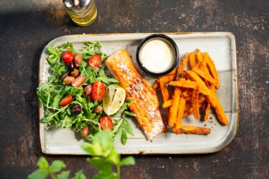 Izgara somon, patates kızartması ve salata. Aşçı yemek pişirir ve iştah açıcı bir yemek servis eder. Tabakta servis edilen bitmiş tabak. Teklif, aşçılık fotoğrafçılığı..