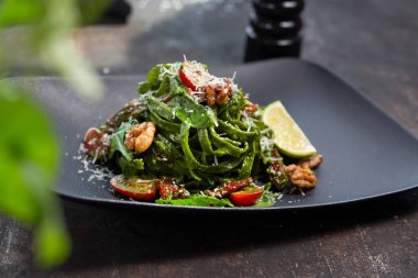 Ispanaklı yeşil spagetti, ceviz, vişneli domates ve parmesan peyniri. Aşçı yemek pişirir ve meze servisi yapar. Tabakta servis edilen bitmiş tabak. Teklif, aşçılık fotoğrafçılığı..