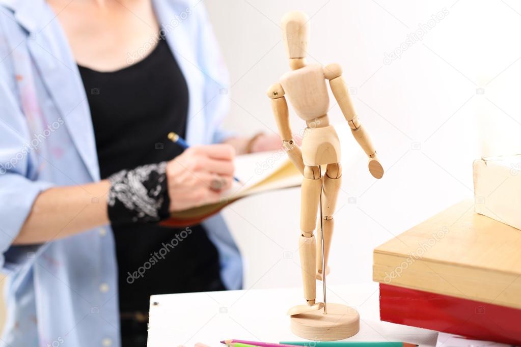 The artist sketches the figure using wooden dummy