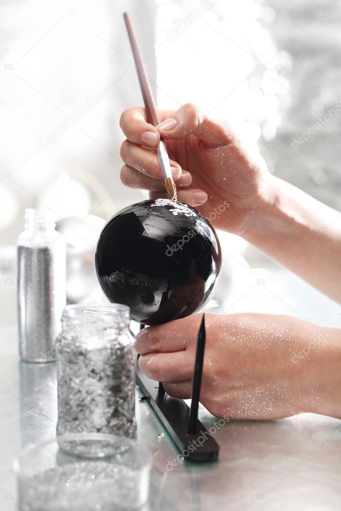 A woman painting a design on a silver bauble