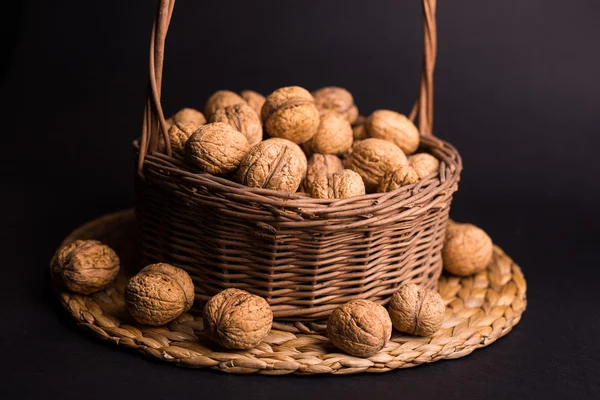 Weidenkorb mit Walnüssen auf schwarzem Hintergrund — Stockfoto