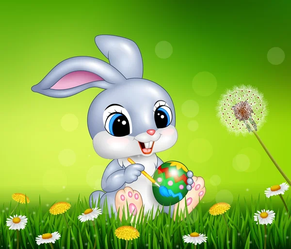 Easter bunny painting an egg on grass background — Stock Vector